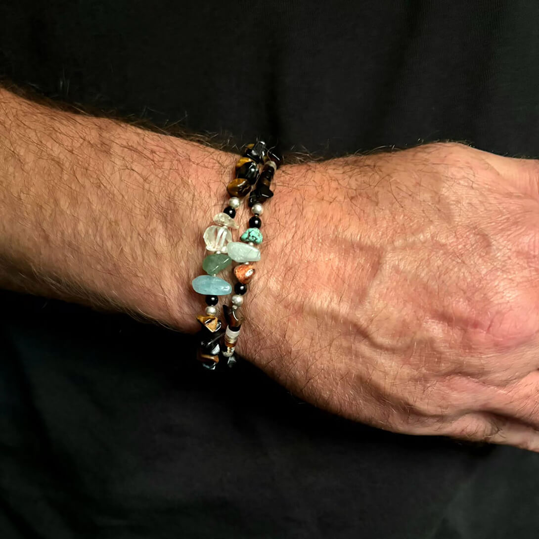 A mans arm wearing two gemstone bracelets